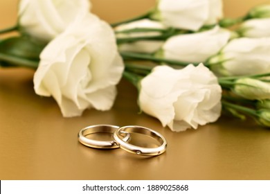 Two golden wedding rings with white roses on a gold background stock images. Engagement rings with a bouquet of white flowers image. Romantic golden wedding background photo