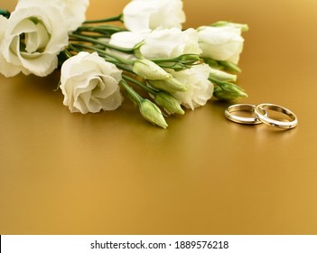 Two golden wedding rings with white flowers on a gold background