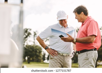 Two golf player standing together using mobile phone. Senior golfers looking the scores on phone after the game on the golf course.