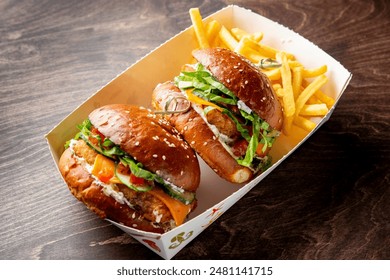 Two gourmet burgers with fresh toppings and fries in a takeout box on a wooden table - Powered by Shutterstock