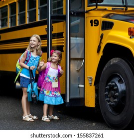 Two Grade School Girls Getting On School Bus For First Day Of School.