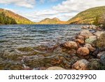 Two granite mountain peaks, called The Bubbles, in Acadia National Park, are bathed in sunlight and autumn foliage color across Jordan Pond on a partly cloudy fall day in Down East Maine.