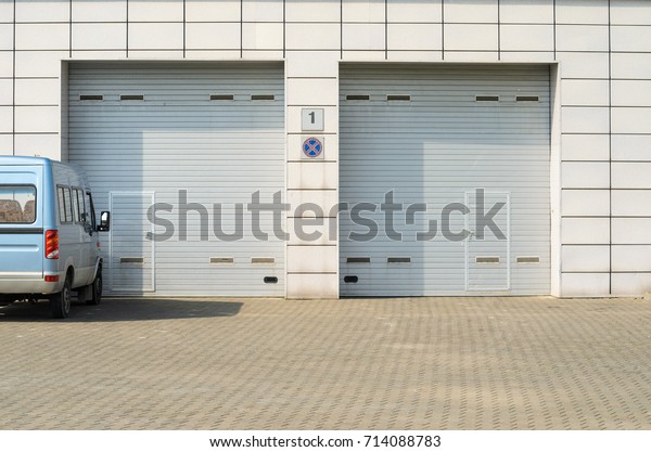 Two\
gray garage doors and a parked minibus. Large automatic up and over\
garage doors with inclusion of smaller personal\
door.