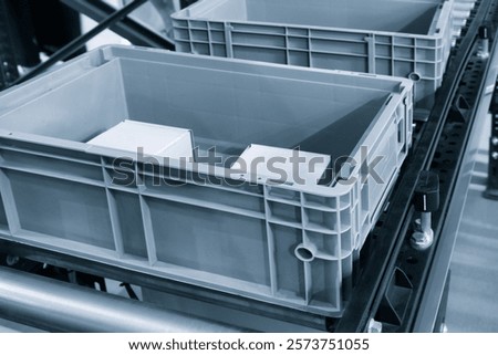 Two gray plastic containers on a conveyor belt. The containers are empty and are waiting to be filled