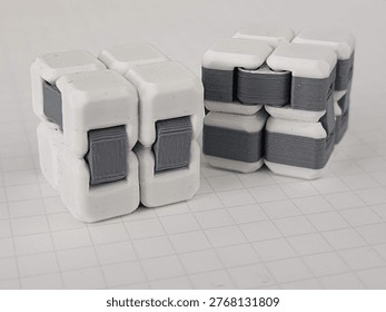 Two gray and white 3D-printed infinity cubes on paper