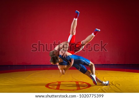 Two greco-roman  wrestlers in red and blue uniform wrestling  on a yellow wrestling carpet in the gym