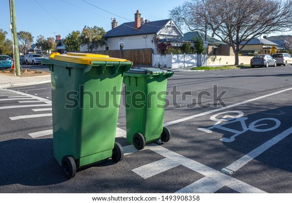 Two green household garbage bins placed on a\
clean suburban street with a view of some residential houses in\
distance. Melbourne, VIC\
Australia.
