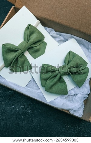Two green linen bow ties displayed on white cards, one on elastic band and one clipped, styled in a gift box. Elegant handmade accessories in soft natural colors for kids or special occasions.