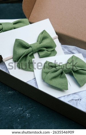 Two green linen bow ties displayed on white cards, one on elastic band and one clipped, styled in a gift box. Elegant handmade accessories in soft natural colors for kids or special occasions.