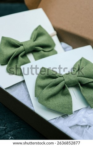 Two green linen bow ties displayed on white cards, one on elastic band and one clipped, styled in a gift box. Elegant handmade accessories in soft natural colors for kids or special occasions.