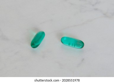 Two Green Pills Close-up On A White Table. Vitamins, Supplements, Antibiotics, Medications, Emergency Care, Painkillers.