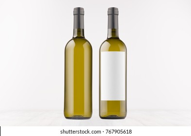 Two green wine bottles with blank white label and without label, on white wooden board, mock up. Template for advertising, design, branding identity.