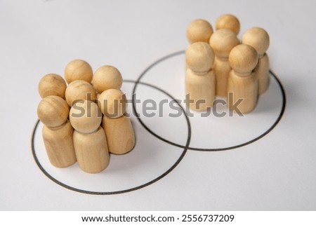 Two groups of wooden figurine are placed within overlapping circles. Merger or acquisition concept.