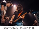 Two guitarists are playing electric guitars on a stage during a concert, illuminated by spotlights, creating an exciting and energetic atmosphere