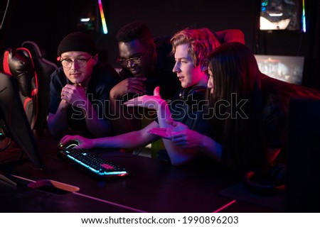 Two guys and a girl in medical masks in a computer club give support to their friend during his game