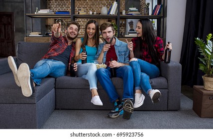 Two Guys And Two Girls Are Relaxing At Home On The Couch Watching A Movie