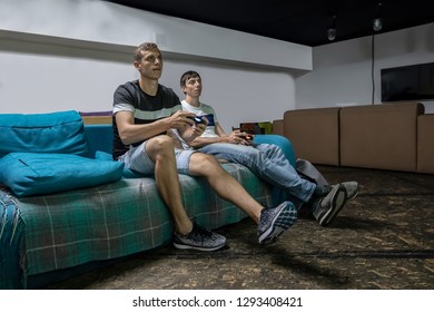 Two Guys Playing On The Console Sitting On The Couch. Portrait Of Two Excited Handsome Men Playing Video Game