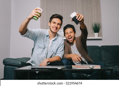 Two guys playing on the console sitting on the couch. European and African friends had a party. victory celebration - Powered by Shutterstock