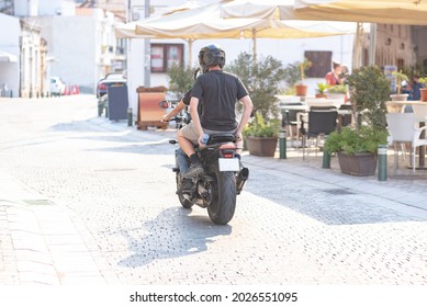 Two Guys Ride A Sports Motorcycle Through The City Streets On A Sunny Day, Rear View.