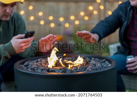 Two guys sitting around a backyard fire pit in autumn