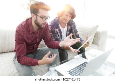 Two Guys Sitting On The Couch And Looking At The Laptop Screen.