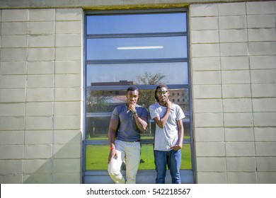 Two Guys standing together posing outside on a sunny day, leaning against mirror on wall in front of green grass and blue sky