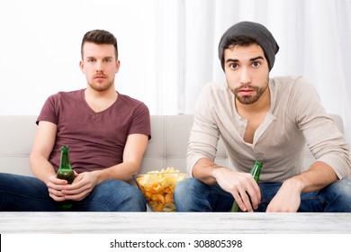 Two Guys Watching Tv, Drinking Beer, Eating Crisps At Home 