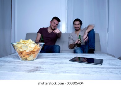 Two Guys Watching Tv, Drinking Beer, Eating Crisps At Home 