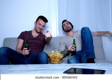 Two Guys Watching Tv, Drinking Beer, Eating Crisps At Home
