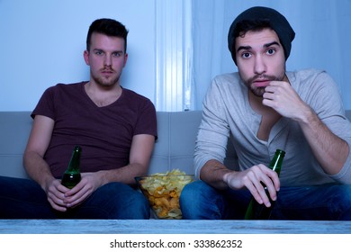 Two Guys Watching Tv, Drinking Beer, Eating Crisps At Home
