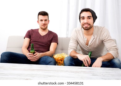 Two Guys Watching Tv, Drinking Beer, Eating Crisps At Home
