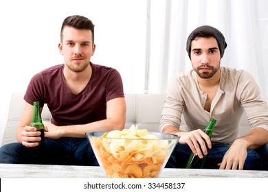 Two Guys Watching Tv, Drinking Beer, Eating Crisps At Home
