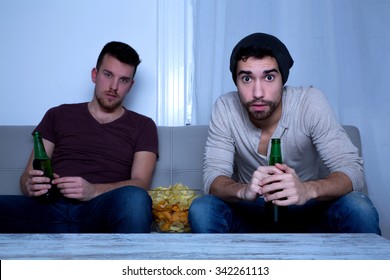 Two Guys Watching Tv, Drinking Beer, Eating Crisps At Home
