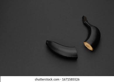 Two halves of a black banana on the matte black background. Minimal style. Conceptual minimalist black art. Matte surface. Cut fruit. One. Space for text