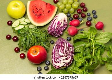 Two Halves Of Blue Cabbage, An Apple, Bunch Of Arugula, Sprigs Of Green Basil And Berries. Flat Lay. Green Background.