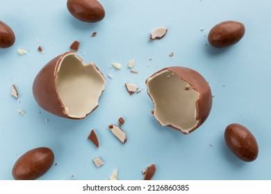 Two Halves Of A Broken Chocolate Egg For Children A Chocolate Egg With Small Eggs Around On A Blue Background. Copy Space In The Middle. Easter Card, Top View.