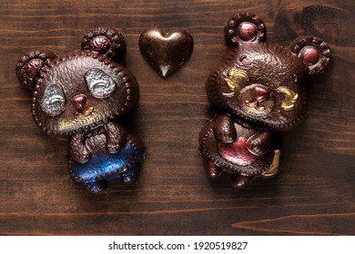 Two Hand Crafted Chocolate Bears And Heart On A Dark Wooden Textured Background