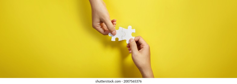 Two hand joining two matching puzzle pieces together in a conceptual image of teamwork and cooperation. - Powered by Shutterstock