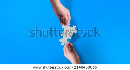 Two hand joining two matching puzzle pieces on blue background, conceptual image of teamwork.