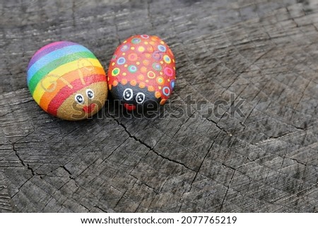 Two hand painted rainbow love bugs on rocks are sitting on a natural wood background.
