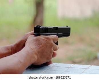 two hand of an unidentified senior male holding and shooting black air soft gun model of a replica real pistol in green area in a garden of a country house with fun and serious mood