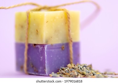 Two Handmade Soaps Tied With String And A Scattering Of Dried Lavendar Shot Against A Lilac Plain Background