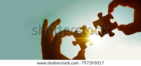 two hands of businessman to connect couple puzzle piece with sky background.Jigsaw alone wooden puzzle against sun rays.one part of whole.symbol of association and connection.business strategy