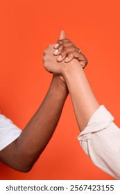 Two hands engaged in a friendly arm wrestling match against a vibrant orange background