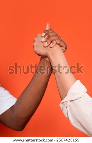 Two hands engaged in a friendly arm wrestling match against a vibrant orange background