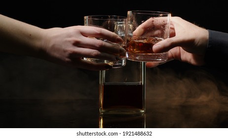 Two Hands With Glasses Of Cognac Whiskey With Ice Cubes Making Cheers On Black Background. Celebration Of Business Success, Christmas, Anniversary, Birthday. Raising Toast With Glasses Of Bourbon, Rum