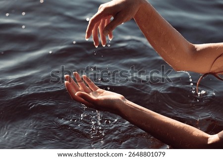 Two hands gracefully splash water in a calm lake on a sunny afternoon, creating ripples and droplets that glisten in the light. atmosphere is tranquil and refreshing.