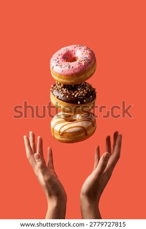 Two hands held open beneath three stacked donuts floating against a coral background