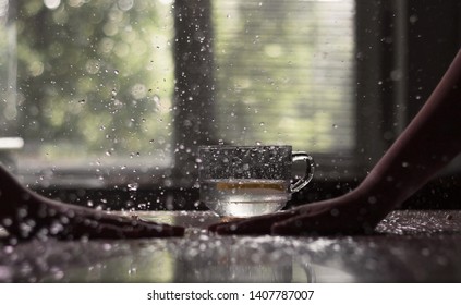 two hands hit the wet table and around a lot of drops. against the background of a glass cup with water and a window