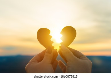 Two hands hold a broken heart on the background of the sunset. Concept spat divorce dissolution, love feelings - Shutterstock ID 1860875815